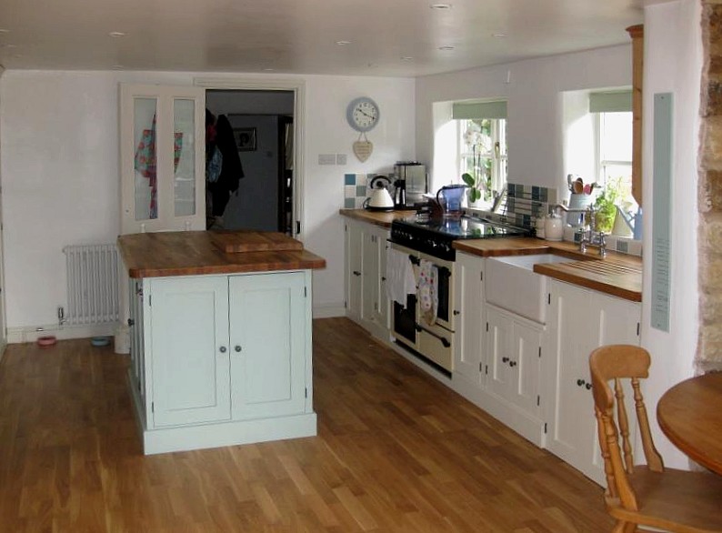 kitchen island painted blue with white painted kitchen units beneath a window